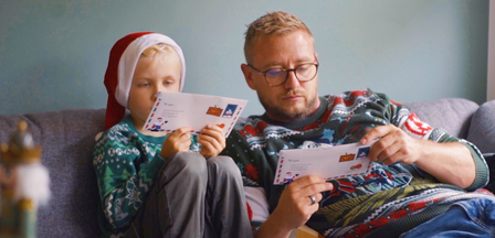 Et close up billede af far og søn som sidder og læser en julehistorie fra Julemandes Posthus